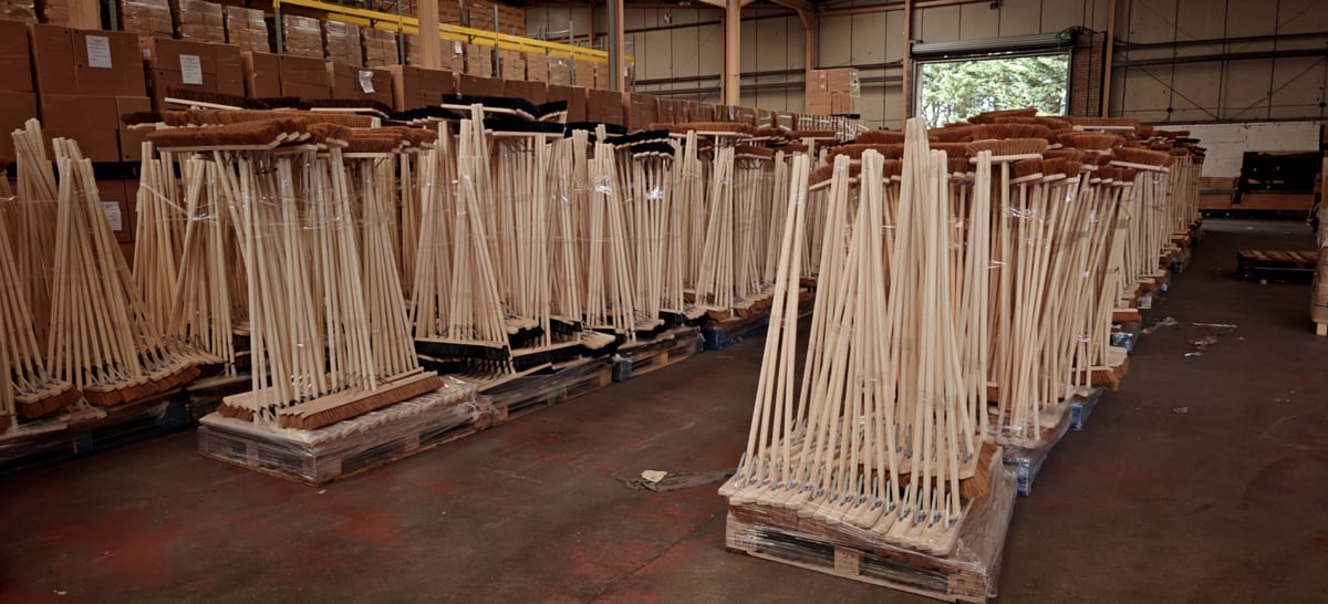 Timber broom handles stacked on pallets in the Sawston warehouse